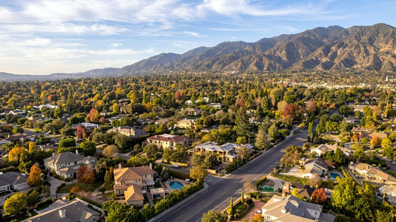 Aerial view of Arcadia estate neighborhoods, tree lined blocks with backyard pools, a wide boulevard toward the mountains.