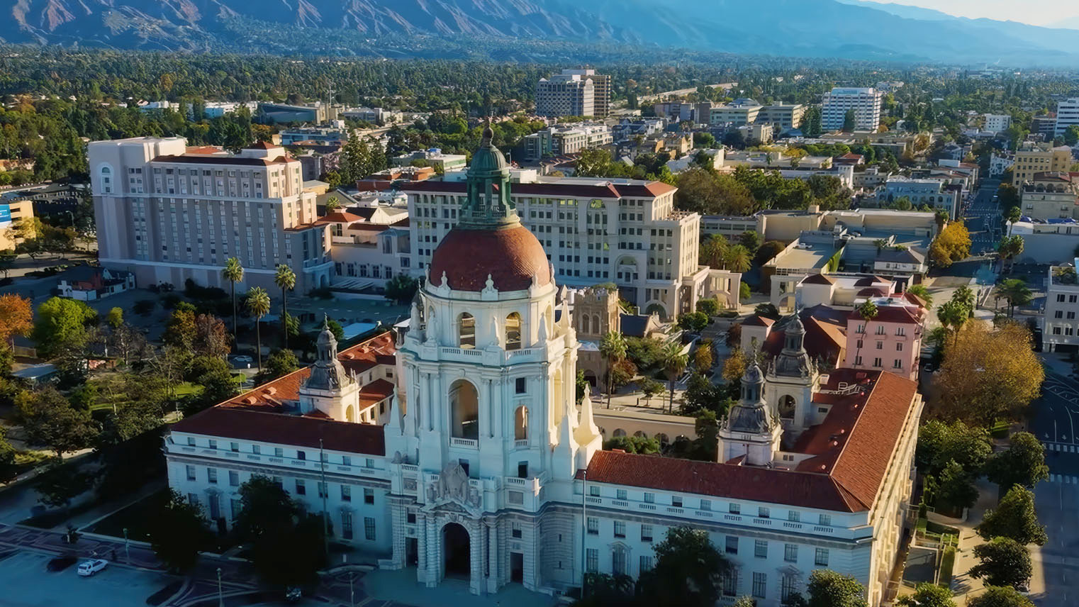 Aerial view of Pasadena City Hall, white baroque tower and red tiled dome above the Civic Center, mountains behind.